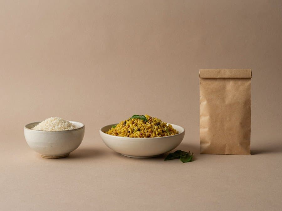 A bowl of rice, a plate of lemon rice and a paper pack of grain